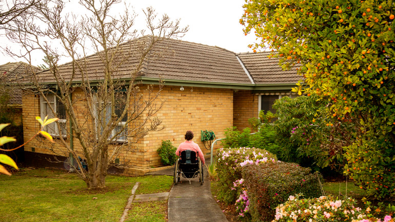 Woman using a wheelchair approaches the front door of her home